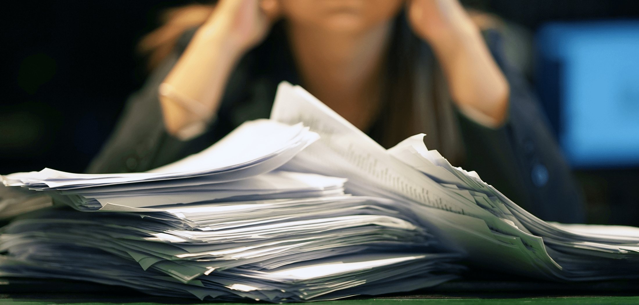 A person holding their head behind a large stack of paperwork