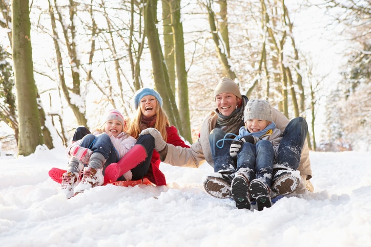 Family Having Fun Sledging Through Snowy Woodland
