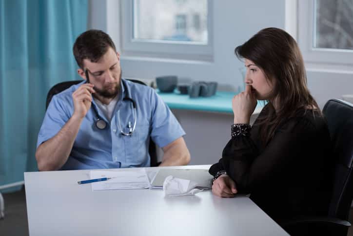 Young worried doctor talking with crying patient's wife